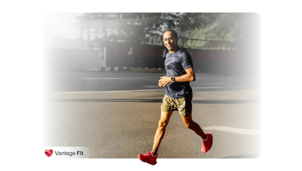 Homme souriant qui fait du jogging à l'extérieur sur un sentier pavé, portant un t-shirt bleu marine et un short vert, regardant une smartwatch à son poignet, avec des arbres en arrière-plan par une journée ensoleillée.webp