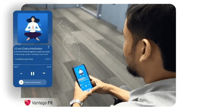 L'image montre une personne utilisant l'application Vantage Fit sur son smartphone, s'engageant dans une session de méditation chakra de 15 minutes. L'utilisateur semble écouter la méditation tout en étant assis dans un environnement de bureau. L'interface du téléphone affiche le minuteur et la barre de progression de la session, ainsi qu'une image d'une personne qui médite..webp