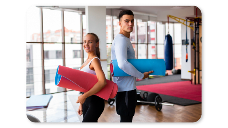 Dos compañeros de trabajo con esterillas de yoga en el gimnasio de la empresa, listos para una sesión de actividad física.