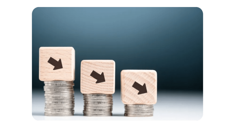 A visual representation of declining financial trends, with wooden blocks featuring downward arrows stacked on top of coins.